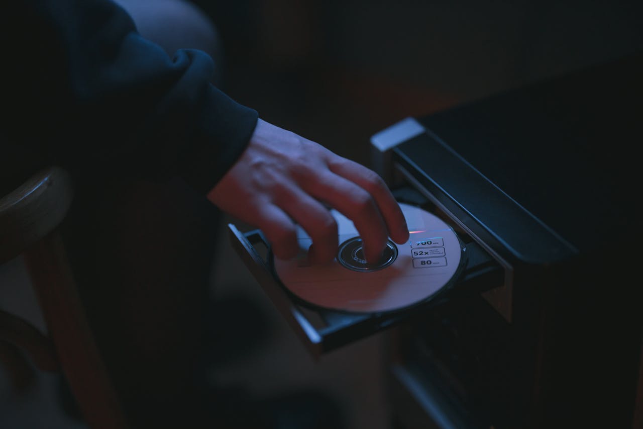 A hand inserting a CD into a computer drive, highlighting cyber security themes.