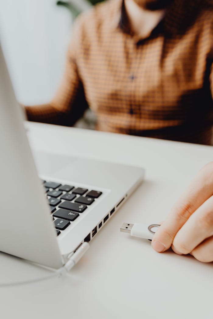 Person inserting a USB flash drive into a laptop port, focused on technology connection.